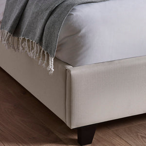 Beige upholstered bed frame with a gray blanket on a wooden floor