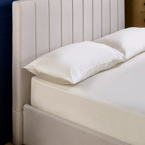 Beige upholstered bed with white pillows against a neutral background