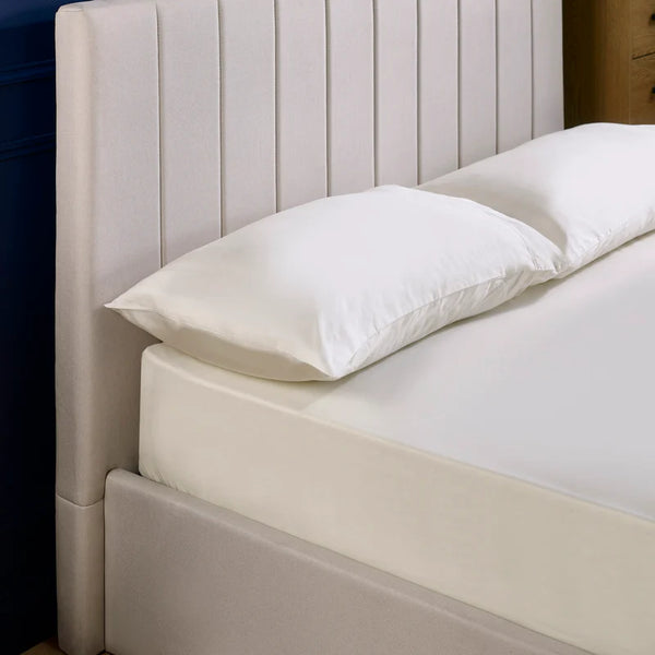 Beige upholstered bed with white pillows against a neutral background
