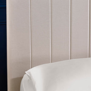Close-up of a beige upholstered headboard with a white pillow.