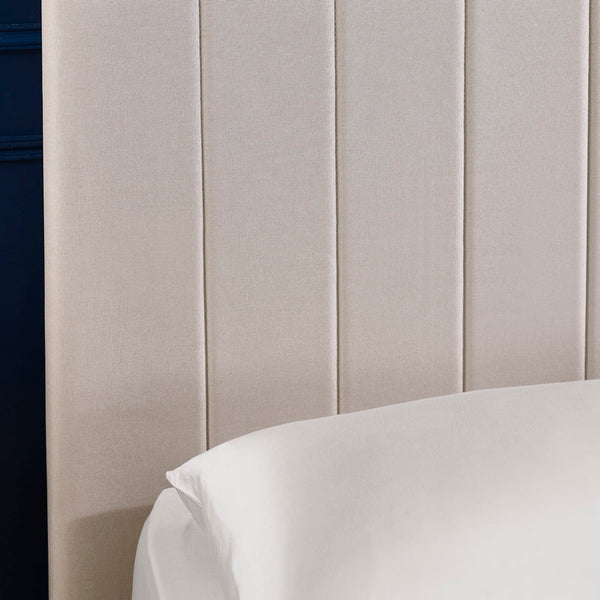 Close-up of a beige upholstered headboard with a white pillow.