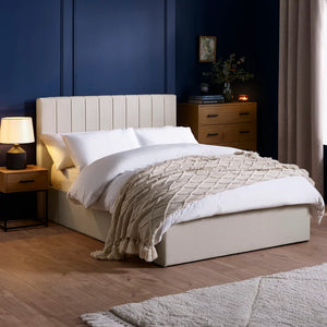 Neatly made bed with beige blanket in a bedroom setting with wooden nightstands and a lamp.