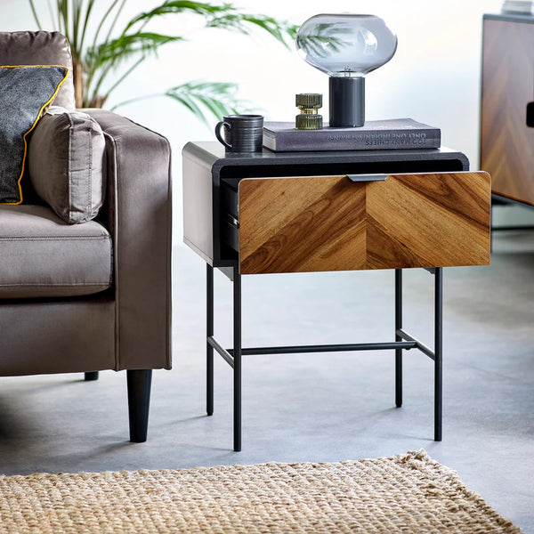 Wooden side table with a lamp and books next to a gray sofa in a living room.