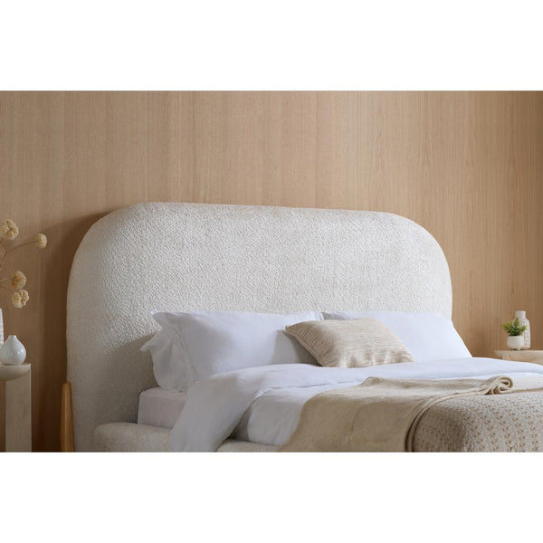 Bed with textured headboard and white bedding against a wooden wall.