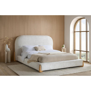 Beige upholstered bed in a modern bedroom with wooden flooring and large window.