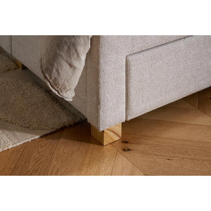 Close-up of a textured bed frame corner with wooden legs on a wooden floor.