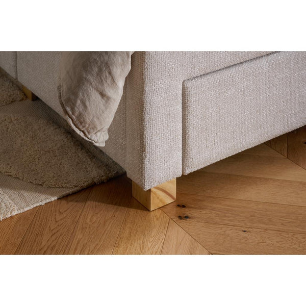 Close-up of a textured bed frame corner with wooden legs on a wooden floor.