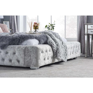 Gray tufted bed with a blanket in a bedroom setting
