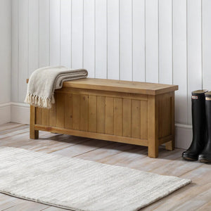 Wooden storage bench with a blanket and boots in a room with white paneled walls and a wooden floor.