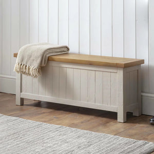 Wooden bench with a blanket draped over it against a white paneled wall.