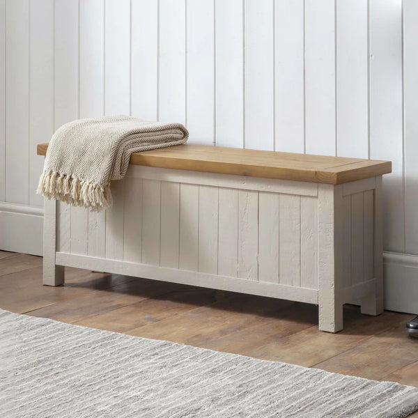 Wooden bench with a blanket draped over it against a white paneled wall.