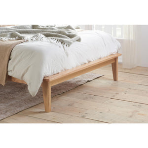 Wooden bed with white bedding and beige blanket on a wooden floor.