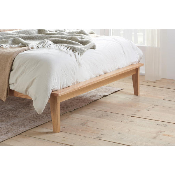 Wooden bed with white bedding and beige blanket on a wooden floor.