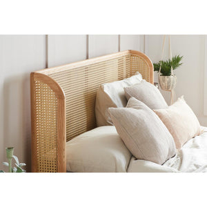 Rattan headboard with pillows on a bed in a room with plants.