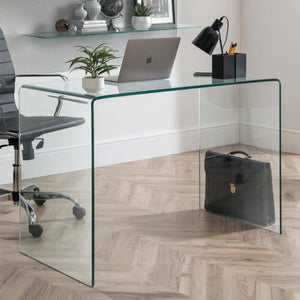 Glass desk with a laptop, plants, and office items in an office setting.
