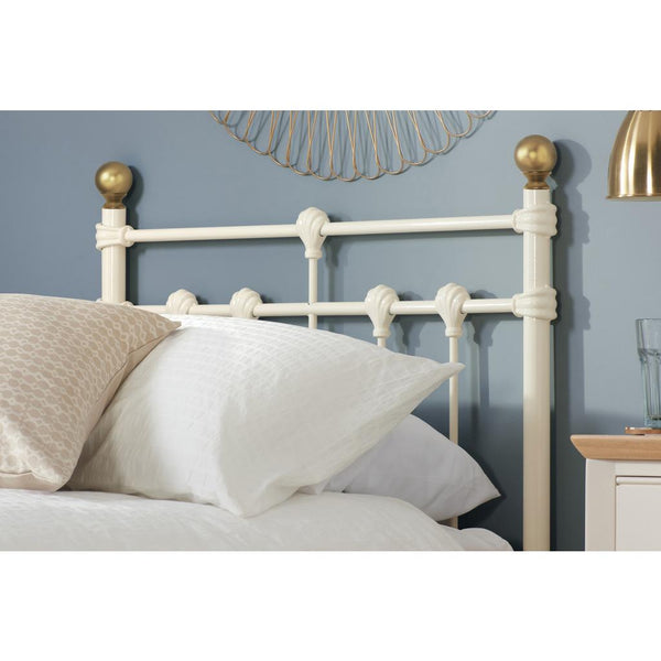White metal headboard with gold accents on a bed against a blue wall.