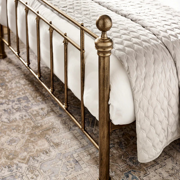 Bronze bed frame with white bedding on a patterned rug