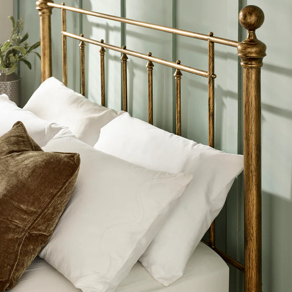 Gold metal headboard with white pillows and a brown pillow against a light green wall.