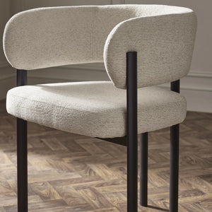 Beige upholstered chair with black metal legs on a wooden floor.