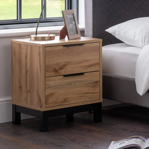 Wooden nightstand with two drawers next to a bed in a bedroom setting.