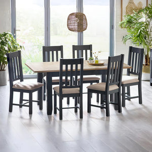 Dining table set with black chairs and beige cushions in a bright room with plants.