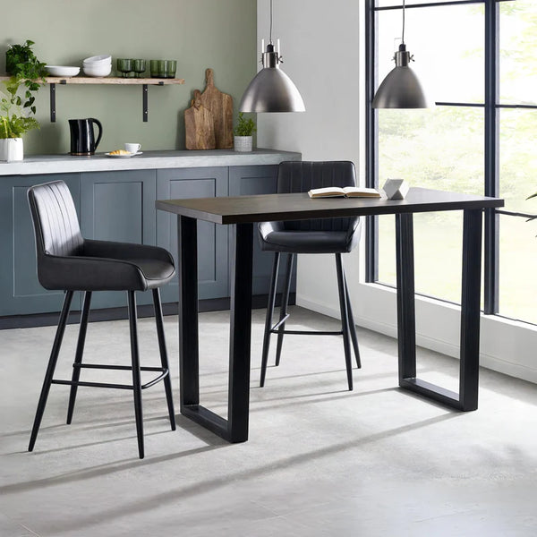 Modern kitchen with a black bar table and bar stools, featuring a green wall and large windows.
