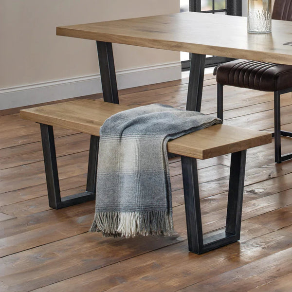 Wooden bench with a plaid blanket draped over it, placed in front of a dining table.