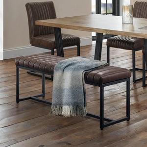 Dining area with wooden table, brown chairs, and a bench with a blanket on a wooden floor.