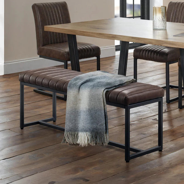 Dining area with wooden table, brown chairs, and a bench with a blanket on a wooden floor.