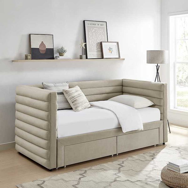 Beige upholstered daybed with white bedding in a room with a shelf and lamp.