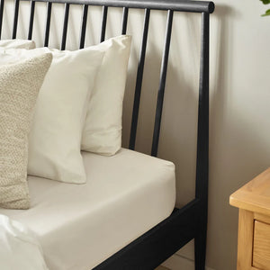 Black metal bed frame with white bedding and pillows against a neutral wall.