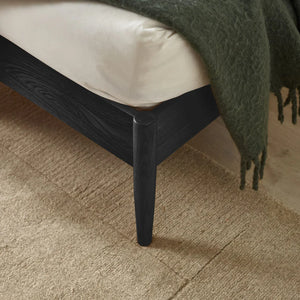 Close-up of a black bed frame with a green blanket on a beige carpet