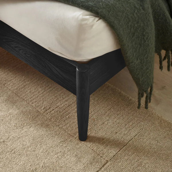 Close-up of a black bed frame with a green blanket on a beige carpet