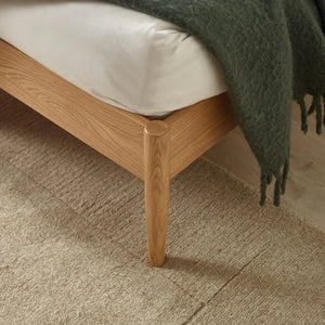 Wooden bed frame with a green blanket on a carpeted floor