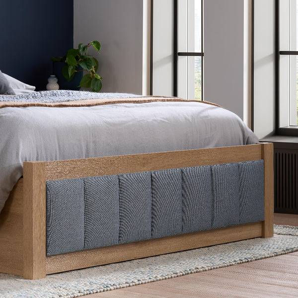 Wooden bed frame with gray upholstered headboard in a bedroom setting.
