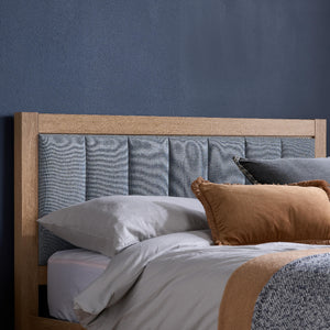 Bed with wooden headboard, gray upholstered panel, and brown and white bedding against a blue wall.
