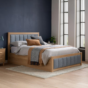 Wooden bed with gray upholstered headboard and bedding in a bedroom setting.