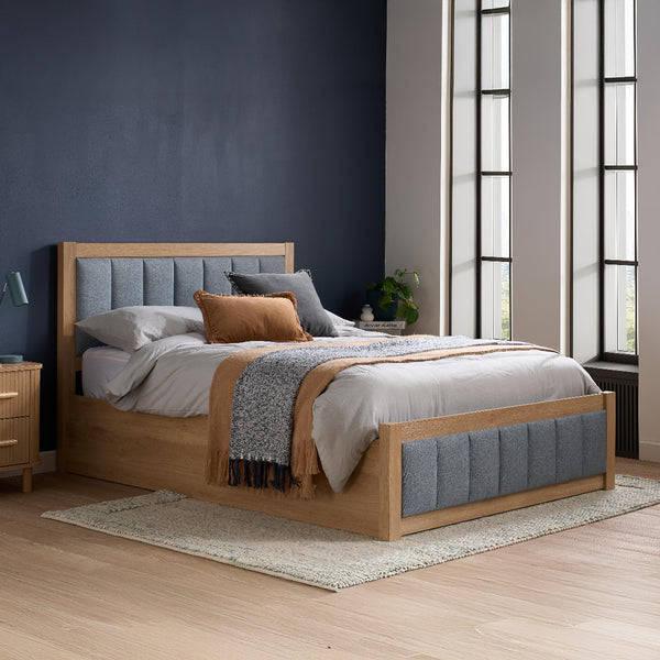 Wooden bed with gray upholstered headboard and bedding in a bedroom setting.
