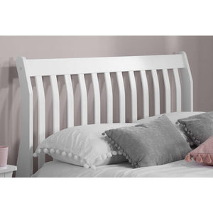 White wooden bed with gray and pink pillows against a plain background