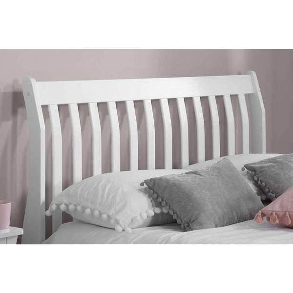 White wooden bed with gray and pink pillows against a plain background