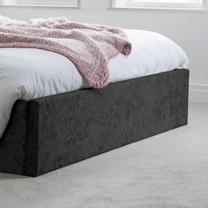 Bed with white bedding and a pink blanket on a dark upholstered bed frame in a room.
