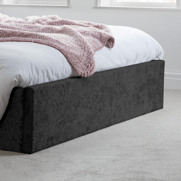 Bed with white bedding and a pink blanket on a dark upholstered bed frame in a room.