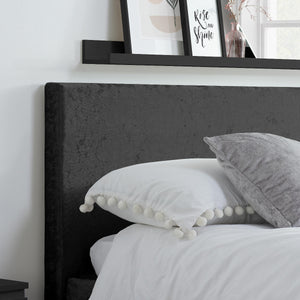 Bed with dark upholstered headboard and decorative pillows, with a shelf above featuring framed pictures.