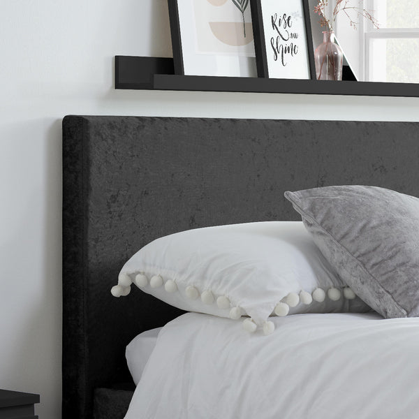 Bed with dark upholstered headboard and decorative pillows, with a shelf above featuring framed pictures.