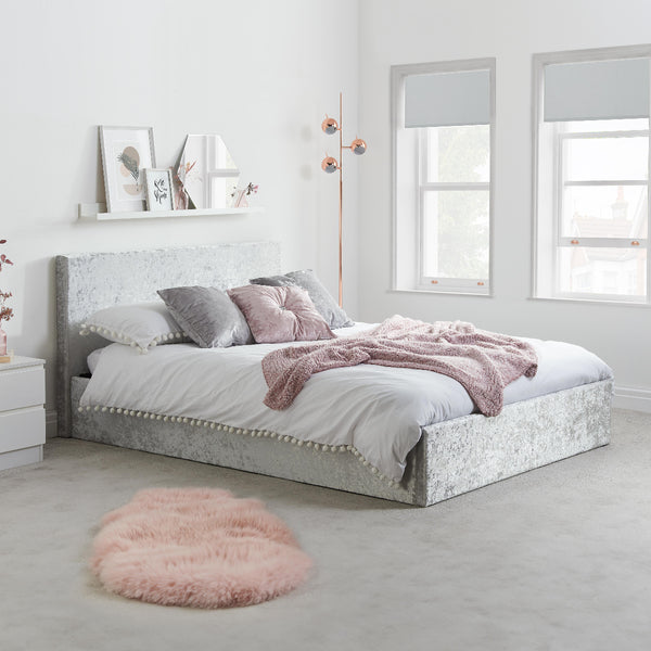 Bedroom with a bed featuring gray and pink bedding, a fluffy pink rug on the floor, and a shelf with decorative items.