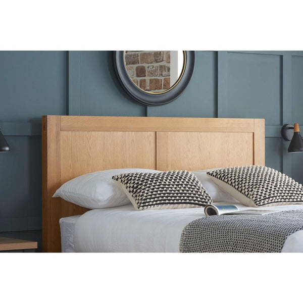 Wooden headboard with bedding and pillows against a gray wall.