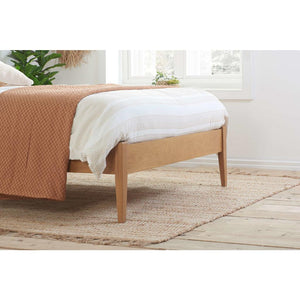 Wooden bed with beige blanket and white pillow in a room with a window and plants.
