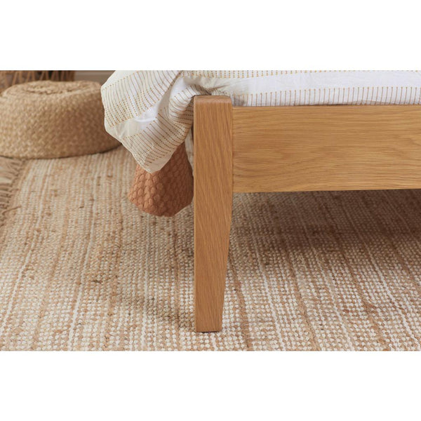 Wooden bed frame with a textured rug and pillow in the background