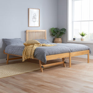 Wooden bed with gray bedding and yellow blanket in a room with a window and plant.