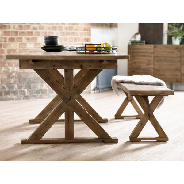 Wooden bench with X-shaped legs in a room with a brick wall and wooden table
